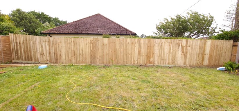 A grassy yard with a wooden fence and a house in the background.