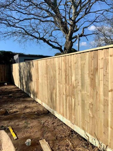 Wooden fence extending along a plot, with a tree and clear blue sky in the background.