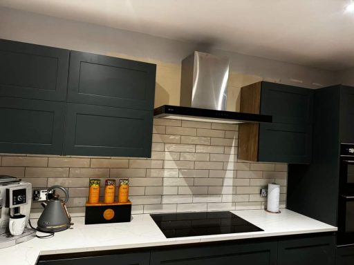 Modern kitchen with dark cabinets, stainless steel extractor hood, and white tiled splashback.