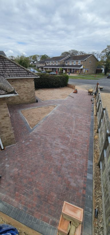 Paved driveway and front garden in a residential area under a cloudy sky.
