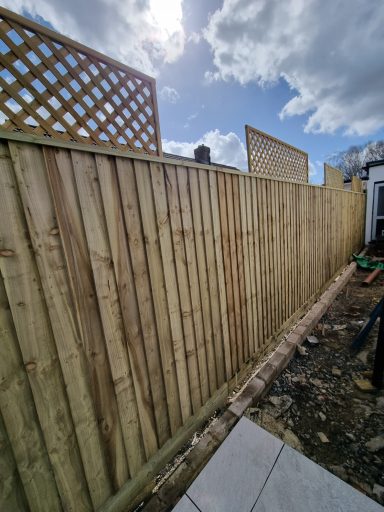 Wooden fence with a trellis on top, under a cloudy sky.