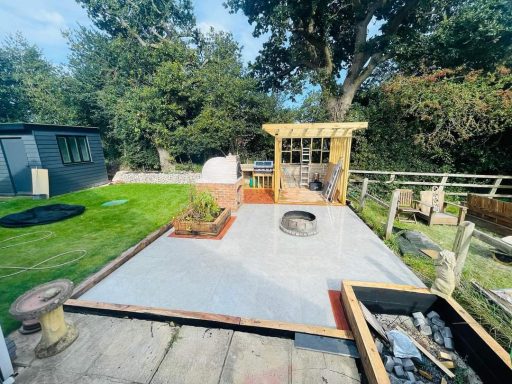 A landscaped garden area with a newly laid patio, seating structure, and greenery.