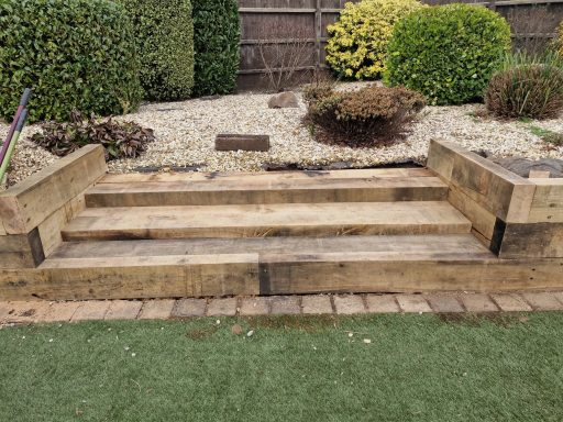Wooden steps in a garden, surrounded by shrubs and a gravel pathway.