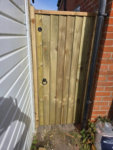 Wooden gate with two circular handles, set between brick and wooden walls.