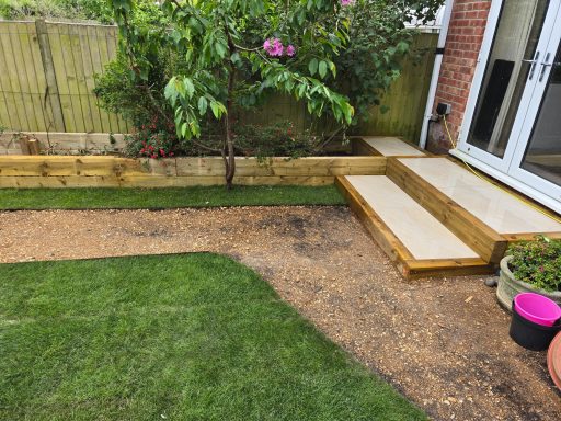 Garden area featuring wooden steps, lawn, and flower pots against a brick wall.