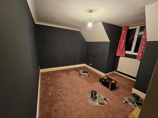 Empty room with grey walls, a pink curtain, and tools on the carpeted floor.