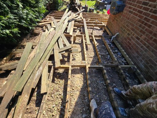 Wooden planks scattered across a construction area, with greenery and a brick wall nearby.