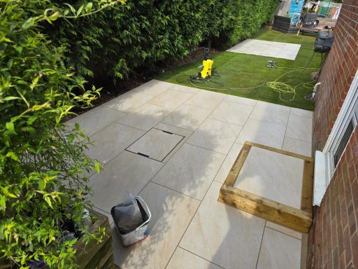 Garden area with tiled patio, bordered by greenery and construction materials.
